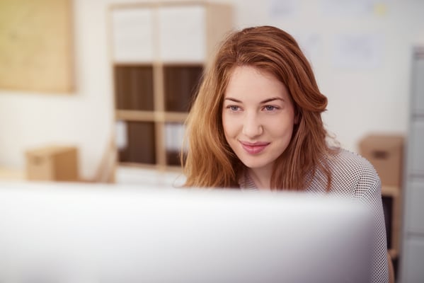 Young woman smiling as she reads text on a desktop computer