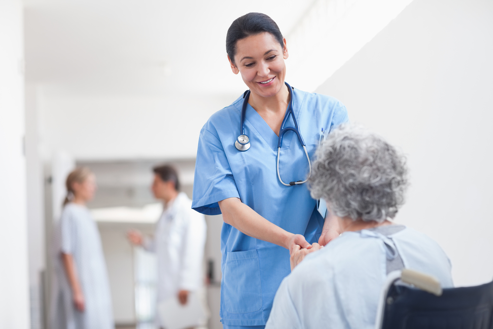 Nurse standing next to a patient while holding her hands in hospital ward