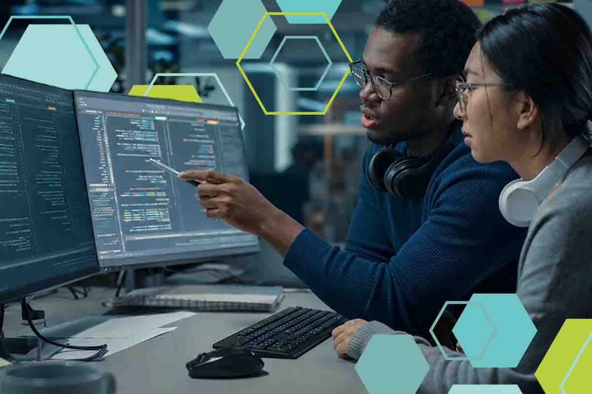 Two software engineers reviewing code together on dual monitors in an office